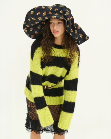 Model wearing a striped yellow and black oversized sweater with an oversized hat