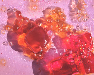 Abstract close-up view of shimmering pink and red liquids swirling together with clusters of glistening clear bubbles