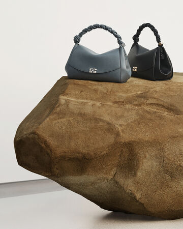 Product display photo featuring a grey bag and a black bag sitting on a large rough rock formation against a minimalist background