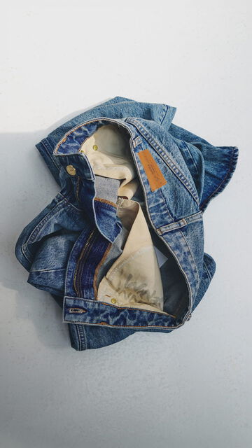 Explore The GANNI Denim Guide to find your perfect jeans fit, featuring a pair of folded blue denim jeans resting on a white surface