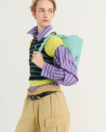 Model wearing a purple stripped shirt layered under a black top and styled with beige pants