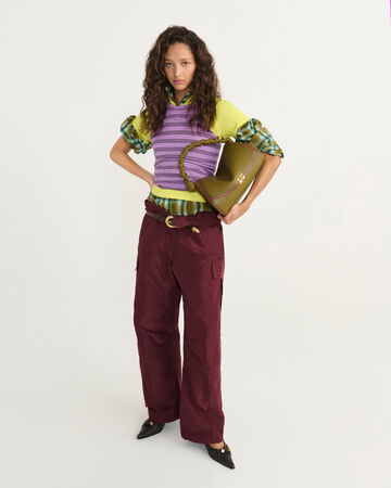 Model wearing a purple top over a checked layered shirt and red pants