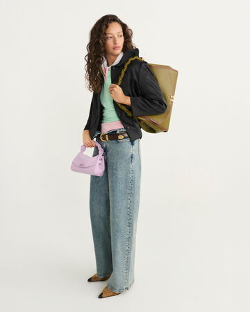 Model wearing a black jacket and blue jeans holding a green shoulder bag
