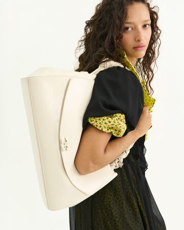 Model wearing a black top and holding a white shoulder bag
