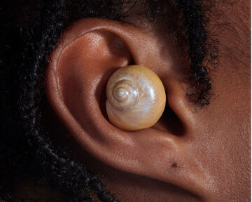 Close-up view of a person's ear wearing a round, smooth cream-colored spiral seashell as an earring