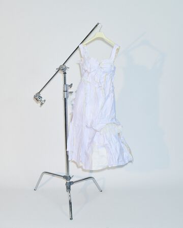 Sisse Bjerre design on rack: A delicate white tiered lace dress hanging on a metal garment stand against a clean studio background