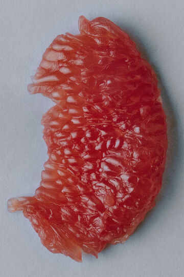 A single isolated wedge of pink grapefruit pulp highlighting its translucent beaded texture against a clean backdrop