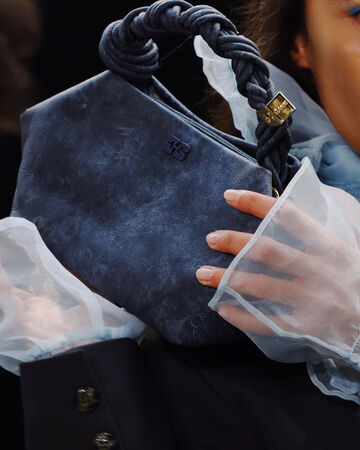 Editorial campaign photo showing a model wearing sheer white tulle gloves holding a dark grey textured Bou Bag close to their chest