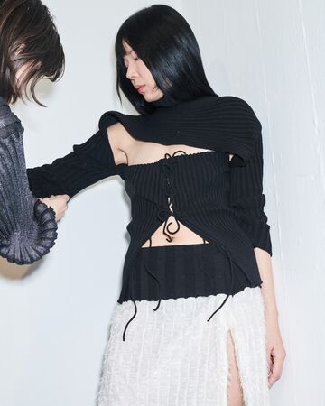 A. Roege Hove design close-up: Side profile view of a model having a black ribbed crop knit top adjusted to showcase texture details