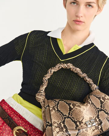 Close-up of model wearing a black knit sweater with a snakeskin handbag
