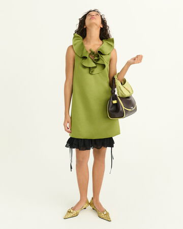 Model wearing a green mini dress with and holding two handbags