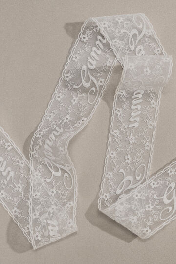 Close-up view of a sheer white lace ribbon patterned with cursive brand script swirling across a neutral background