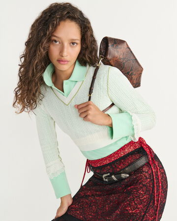 Model wearing a mint green polo collar shirt, patterned skirt, and shoulder bag