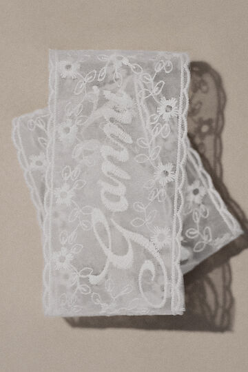 Close-up view of a sheer white lace ribbon patterned with cursive brand script swirling across a neutral background