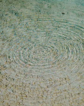 Close-up of textured concentric circles rippling out across a shallow sandy seabed water surface