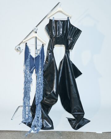 Alectra Rothschild design close-up: A clothing rack holding a pair of light blue patterned denim pants alongside a matching black faux-leather structured corset vest and chaps