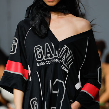 Close-up of a black off-the-shoulder top detailed with fine white abstract line illustrations and bright red cuffs