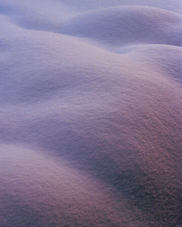 A smooth, minimalist landscape of finely textured sand dunes under a soft purple hue