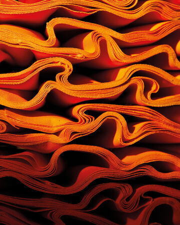 Macro close-up view of layered, wavy orange and yellow textile fibers showing a tightly packed, repeating organic structure
