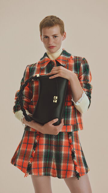 Model standing in a an orange checked jacket and skirt holding a black Very Bou bag