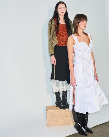 Sisse Bjerre design looks: Two people posing in layered white lace midi dresses styled with patterned earthy-toned tops and black boots