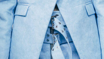Close-up of a light blue leather garment with silver buckle and eyelet detailing