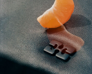 lose-up view of an orange fruit slice resting on a textured dark surface next to a heavy, dark metallic component