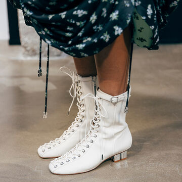 Close-up view of white lace-up boots decorated with eyelets and buckle details, styled beneath a dark patterned skirt hem