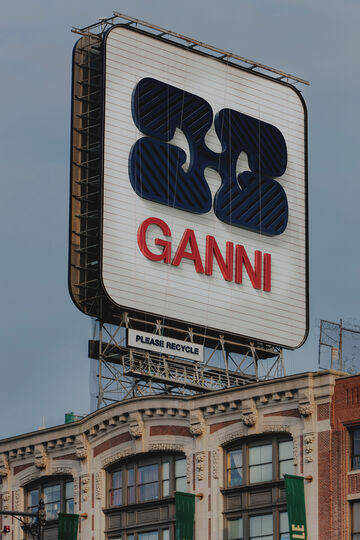 A retro rooftop billboard featuring the GANNI logo against a blue sky