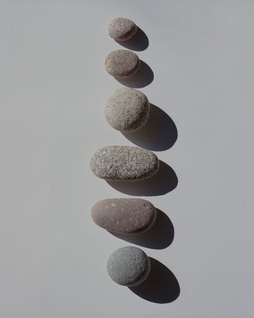 A row of seven smooth, rounded grey stones arranged from largest to smallest casting sharp shadows on a plain white surface