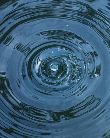 Top-down close-up view of clear blue water rippling out in concentric circular waves around a splash