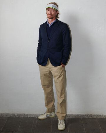 Nicolaj Reffstrup standing and wearing a navy blazer and beige trousers